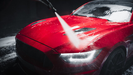 Car Wash Expert Using Water Pressure Washer to Rinse a Red Modern Sportscar. Adult Man Washing Away...