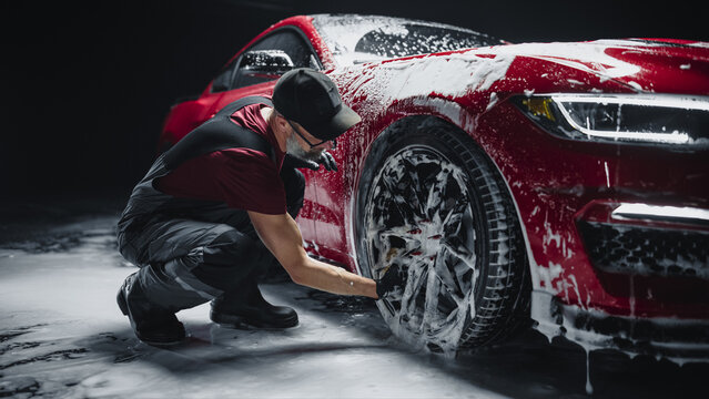 Red Sportscar's Wheels Covered in Shampoo Being Rubbed by a Soft Sponge at a Stylish Dealership Car Wash. Performance Vehicle Being Washed in a Detailing Studio