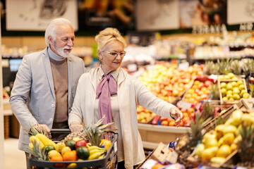 An old healthy couple is purchasing fresh fruits at the supermarket.