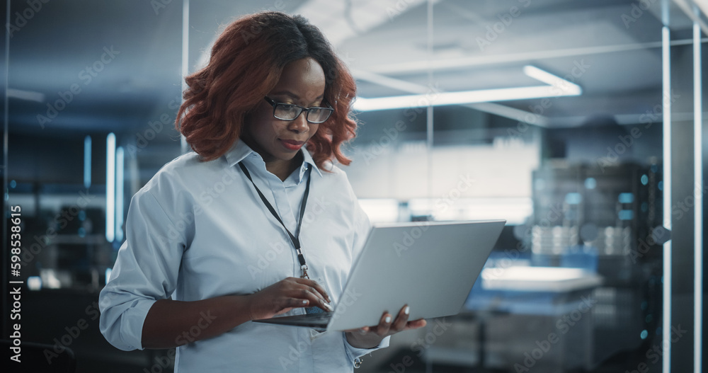 Poster Portrait of a Technological Software Engineering Department Manager Standing and Using a Laptop Computer. African Female Looking in the Distance and Thinking while Working in the Office