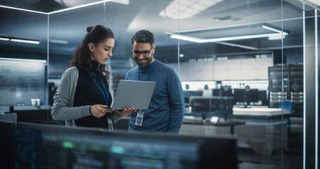 Portrait of Two Happy Female and Male Engineers Using Laptop Computer to Analyze and Discuss How to Proceed with the Artificial Intelligence Software. Casually Chatting in High Tech Research Office