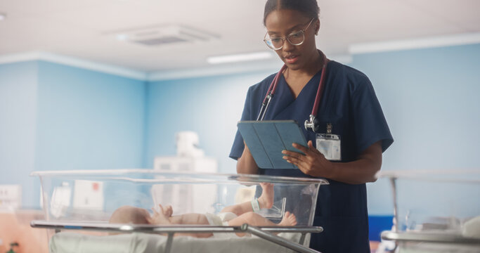 Young African Nurse Using Tablet Computer Checking Up on a Newborn Baby in Maternity Ward Facility. Healthy Infant Lying in a Nursery Clinic, Waiting for Mother to Recover After Childbirth