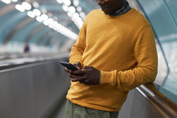 Close-up of African American businessman typing message on smartphone standing on escalator in underground