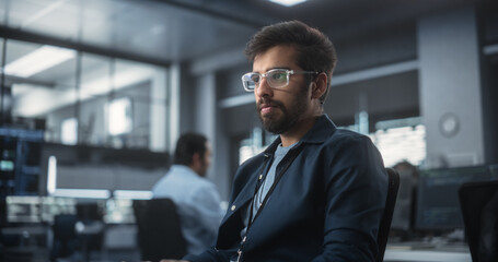 Handsome Indian Software Developer Working on Computer in a Technological Laboratory Environment. Young Man is Thoughtful at His Workplace, Drafting Research Ideas for an AI Development Blockchain