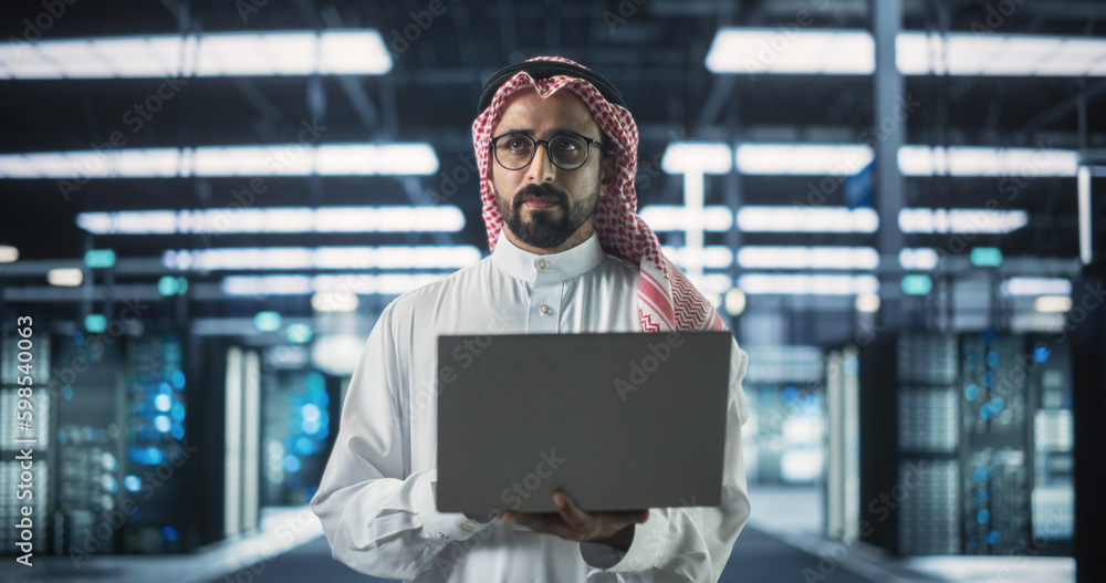 Poster portrait of a muslim data center technical manager wearing traditional white clothes, using laptop c