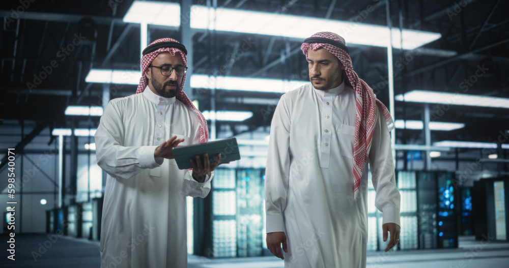 Poster Middle Eastern Computer Engineer and Cybersecurity Specialist Work in Server Room, Talk, Perform System Maintenance Check with Laptop Computer. Specialists Doing Database Diagnostics in Data Center