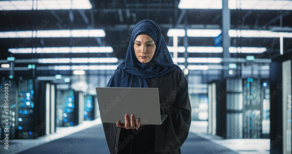 Poster Muslim Female Data Center IT Engineer Standing in a Room with Server Racks. Cloud Computing Architect Uses Laptop Computer for Servicing the System in Cyber Security and Data Protection Facility