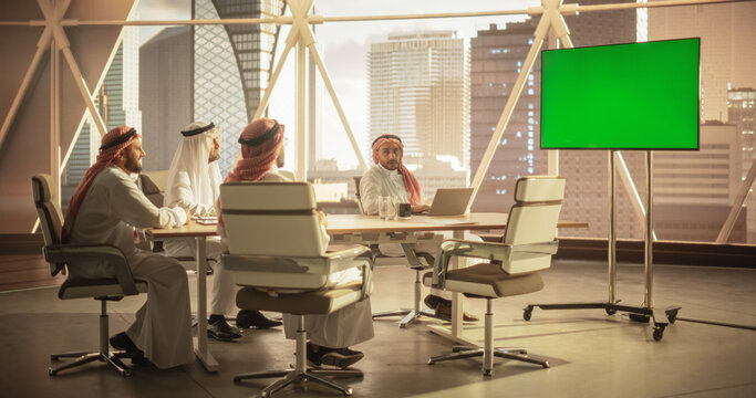 Group of Middle Eastern Executives and Management Having Conference Video Call with a Remote International Office. Businessmen Watching a Presentation on TV with Green Screen Mock Up Display.
