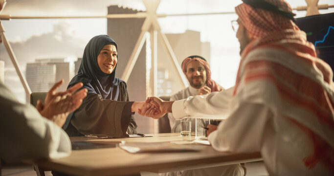 Muslim Businesspeople Closing a Business Deal at a Corporate Modern Office. Female and Male Representatives Shake Hands and Celebrate Successful Partnership. Saudi, Emirati, Arab Office Concept