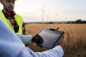 Close up of operator hands holding remote control and quad copter. Male technicians using a tablet drone at work. Engineers controlling data dron in renewable energy windmill field