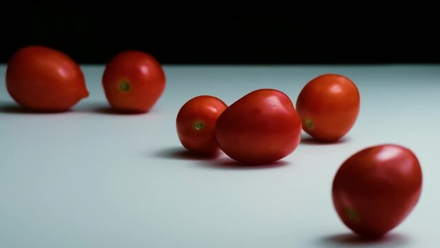 SLOW MOTION FOOD: A large quantity of tomatoes tumble onto a black and white mirrored surface, bouncing and rolling back in a playful, mesmerizing motion