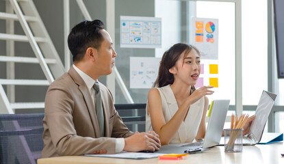 Asian professional successful male businessman manager mentor in formal business suit standing helping teaching supporting female businesswoman colleague sitting working with laptop notebook computer