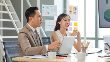 Asian professional successful male businessman manager mentor in formal business suit standing helping teaching supporting female businesswoman colleague sitting working with laptop notebook computer