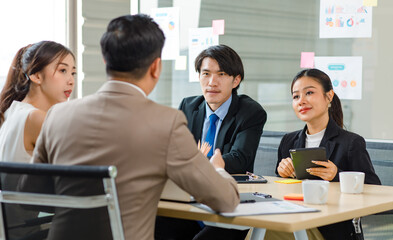 Asian professional successful male businessman manager mentor supervisor in formal business suit sitting helping teaching supporting female businesswoman colleague work with laptop in meeting room.