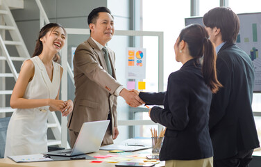 Asian professional successful businesswoman standing smiling shaking hands greeting with unrecognizable businessman in formal business suit while male female colleagues clapping hands celebrating.