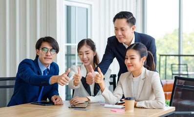Group of successful professional asian businesswoman, businesswoman in formal suit sitting at desk, thumbs up to each other for excellent work.