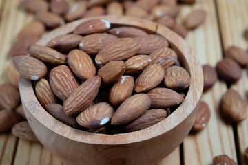 Peeled almonds in a wooden bowl and scattered nuts on a wooden table, top view.	
