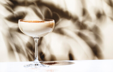 Brandy alexander alcoholic cocktail with cognac, cocoa liquor, cream, grated nutmeg and ice. Light beige background, hard light, shadow pattern