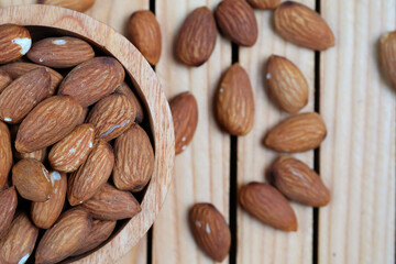 Peeled almonds in a wooden bowl and scattered nuts on a wooden table, top view.	
