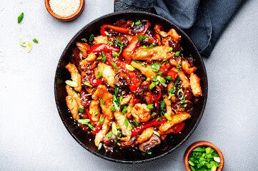 Asian cuisine, stir fry with chicken fillet, red paprika, mushrooms green onion and sesame in frying pan. Gray kitchen table background, top view, copy space