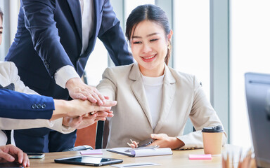 Closeup shot Asian professional successful female businesswoman sitting smiling with unrecognizable male businessmen employee colleagues in formal business suit holding hands stacking unity together