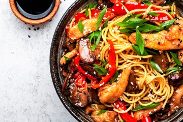 Stir fry noodles with chicken, red paprika, mushrooms, chives and sesame seeds in bowl. Asian cuisine dish. White table background, top view