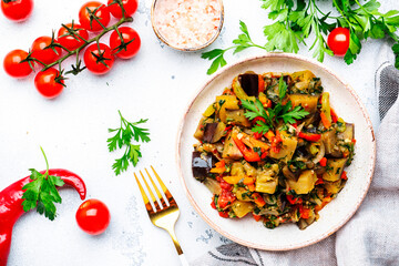 Vegetable stew, saute or caponata. Stewed eggplant with red paprika, tomatoes, garlic, onion, spices and herbs. White kitchen table background, top view