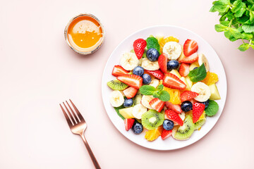 Summer healthy fruit and berry salad with strawberries, blueberries, banana, kiwi, orange and mint leaves, pink background, top view