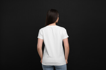 Woman wearing white t-shirt on black background, back view