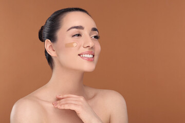 Woman with swatch of foundation on face against brown background. Space for text
