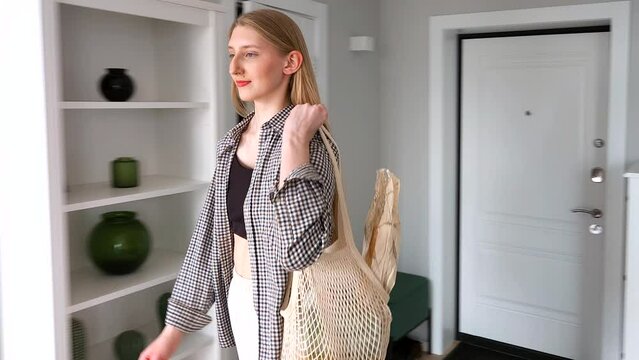 A young woman returns home after shopping carrying healthy food in string bag