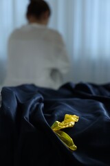 Woman sitting on bed and unrolled condom in bedroom, selective focus. Safe sex