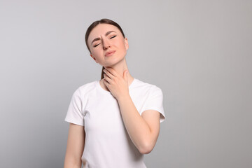 Young woman with sore throat on light grey background