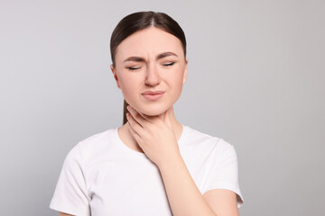 Young woman with sore throat on light grey background
