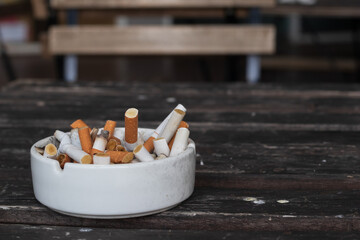 A full ashtray with many cigarette butts put on old dark brown wooden table. Selective focus and copy space. Background for health care or world no tobacco day concept.