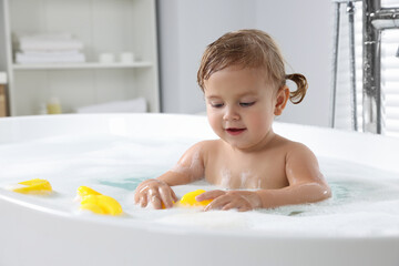 Cute little girl with rubber ducks in foamy bath at home