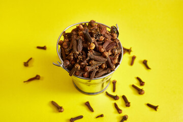 A small metal bucket filled with clove spices on a yellow background.
