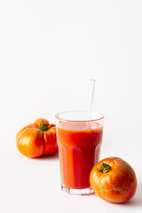 Homemade freshly squeezed tomato juice in a glass with a glass straw and tomatoes on a white background