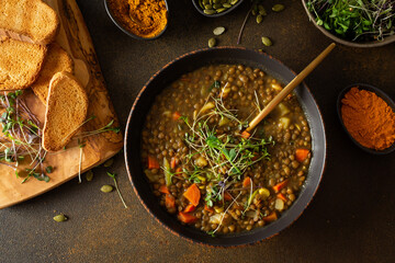 Healthy vegetarian lunches, brown lentil soup with tomatoes and carrots, potatoes and curry spices, toasted croutons, bowl with soup on cutting board on brown background