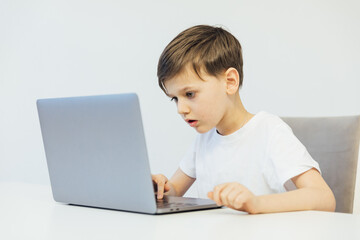 a boy sitting at a laptop at a desk in a classroom education online school