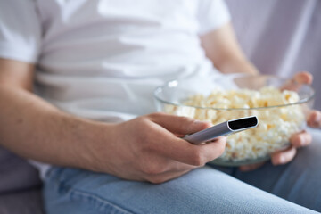 Man watching TV and eating popcorn at home on the couch, front view.