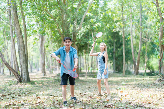 Happy cheerful young asian couple playing badminton game together in the park. urban asian sporty man and woman having fun outdoor sports and game activity concept. picnic and vacation.