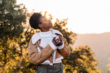 young african woman embraces the outdoors finding peace with tea in the morning, concept of nature's warmth and wilderness lifestyle