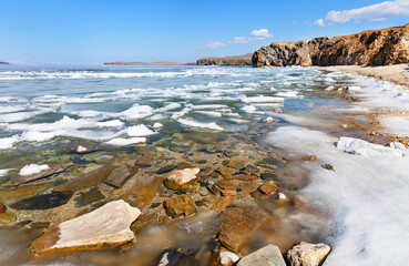 Baikal Lake on sunny May day. Melting ice on beach of Olkhon Island. Through thawed patches with...
