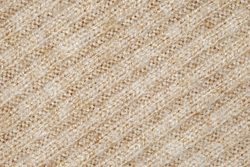 Beige knitted fabric made of yarn threads in close-up, diagonal stitches, uniform texture background