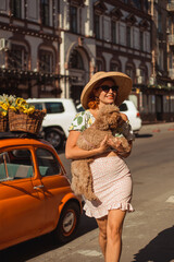 A young beautiful woman in sunglasses walks around the city on a summer day holding her puppy in her arms