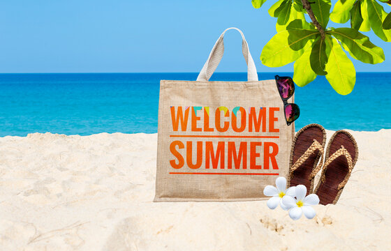 Welcome summer banner on jute bag with handmade jute sandals and sunglasses on tropical beach, summer outdoor day light