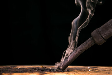 Hot soldering iron with rosin smoke touches wooden board on black background