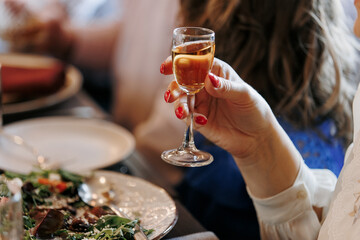 Unrecognisable woman holding glass of alcohol drink, cognac, liquor makes toast by the festive table, fun for a birthday, wedding, anniversary or any other holiday, happy atmosphere, friendly company