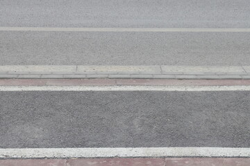A street border painted in white and black on the background of the road and green foliage in the summer closeup. Road safety, minimalism.